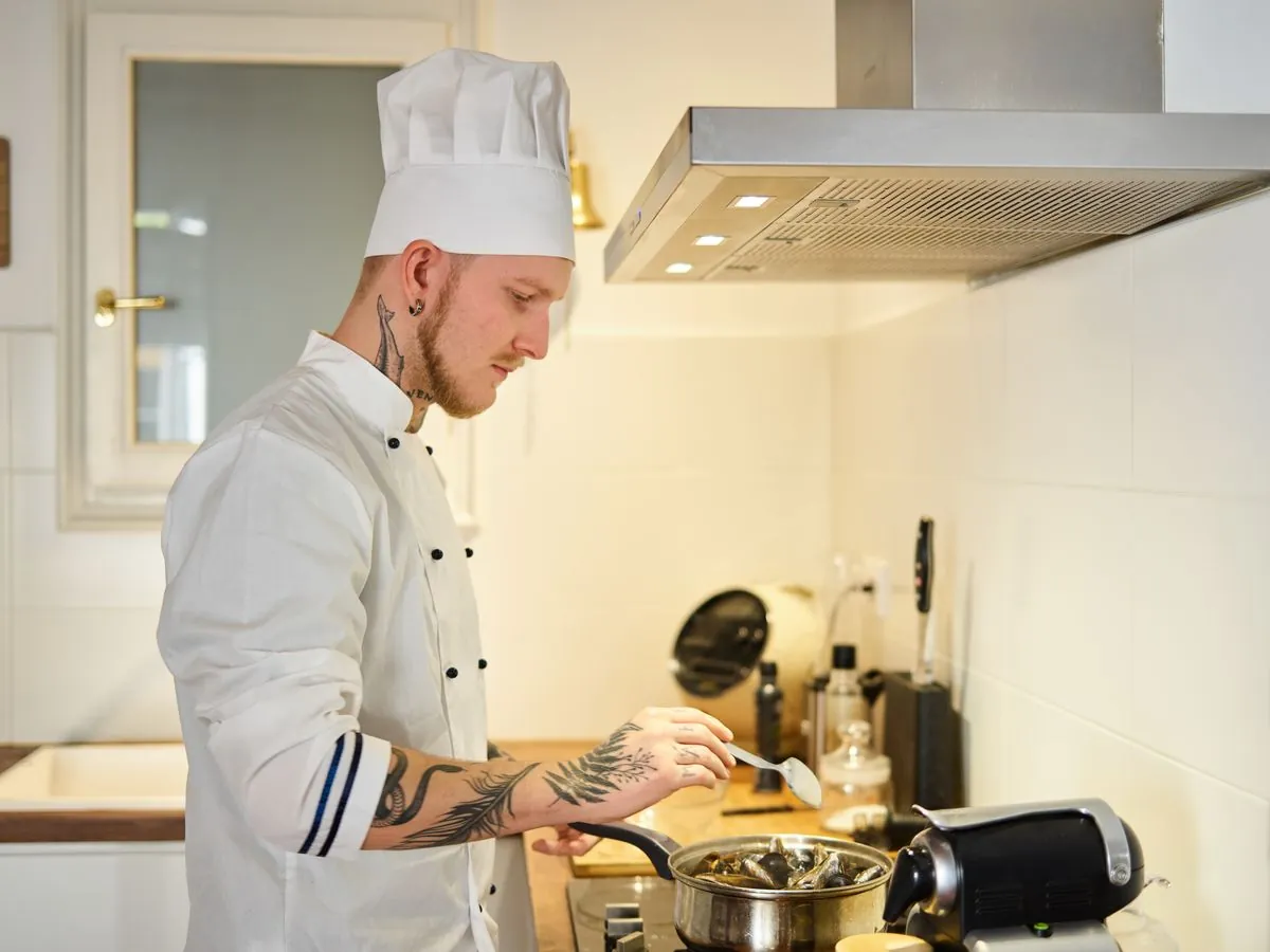Un cuisinier en veste et toque blanches de cuisine prépare un plat dans une cuisine professionnelle