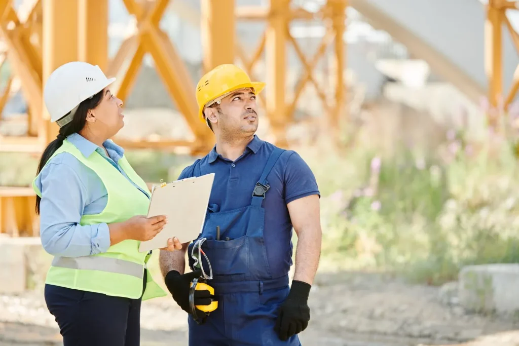 Un ouvrier en tenue de travail bleue avec casque jaune et une collègue en gilet haute visibilité jaune sur un chantier